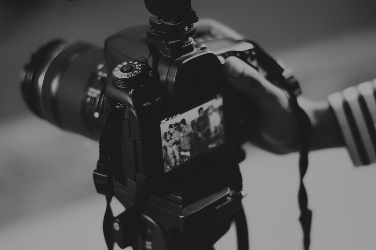 our-story Black and white image of a DSLR camera capturing people in focus, showcasing photography professionalism.