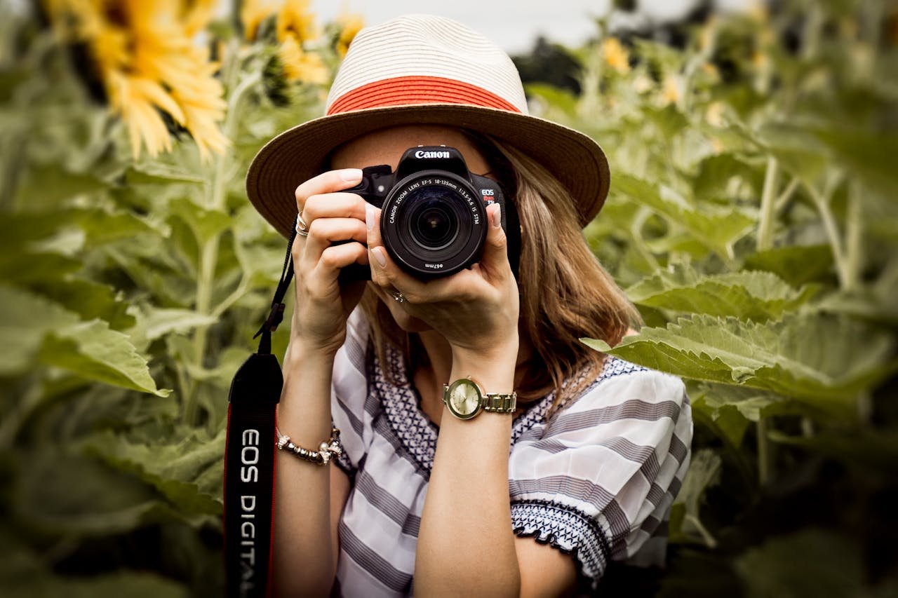 gallery-04 Woman with hat photographing sunflowers in a summer field using a Canon camera.